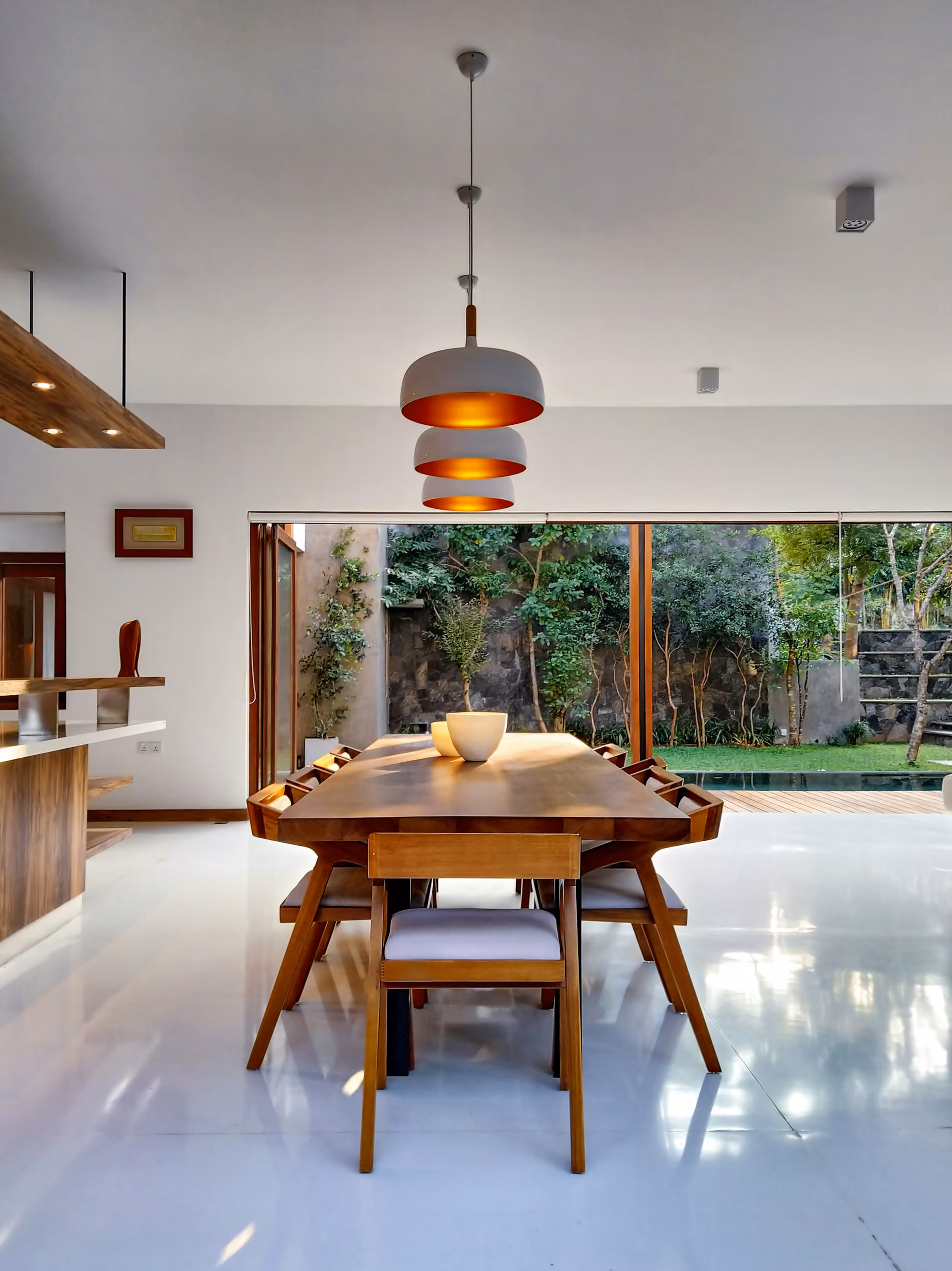 Timber furniture and warm pendant lights frame a leafy courtyard in the architectural imagery used for the MORA concept.